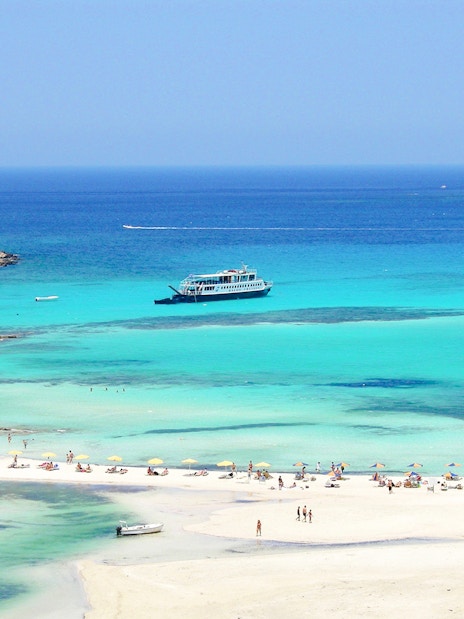 Cruise ship near Balos Island with beachgoers on sandy shore.