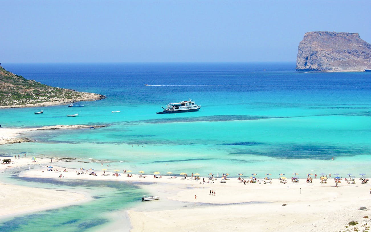 Cruise ship near Balos Island with beachgoers on sandy shore.
