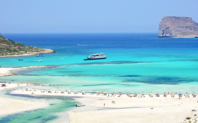 Cruise ship near Balos Island with beachgoers on sandy shore.