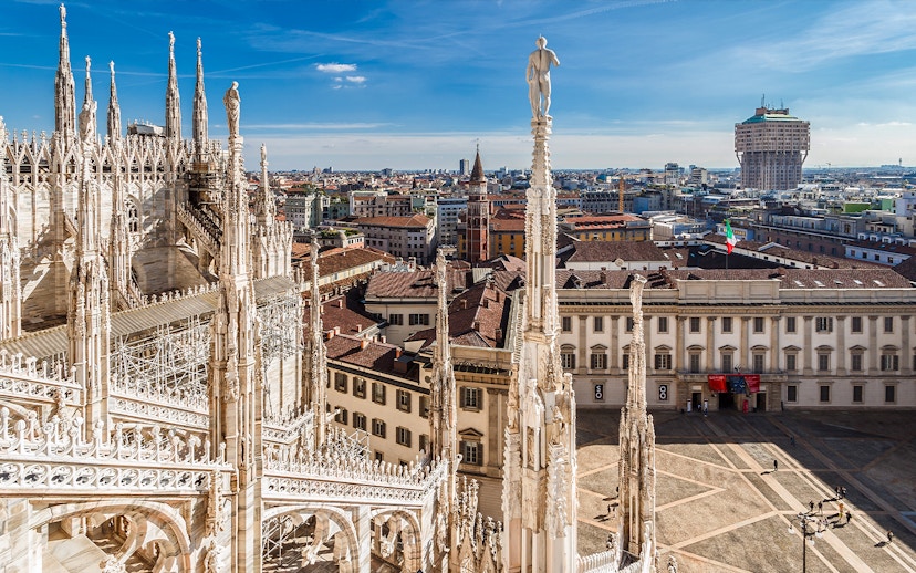 Milan Cathedral rooftop view with cityscape and Italian flag.