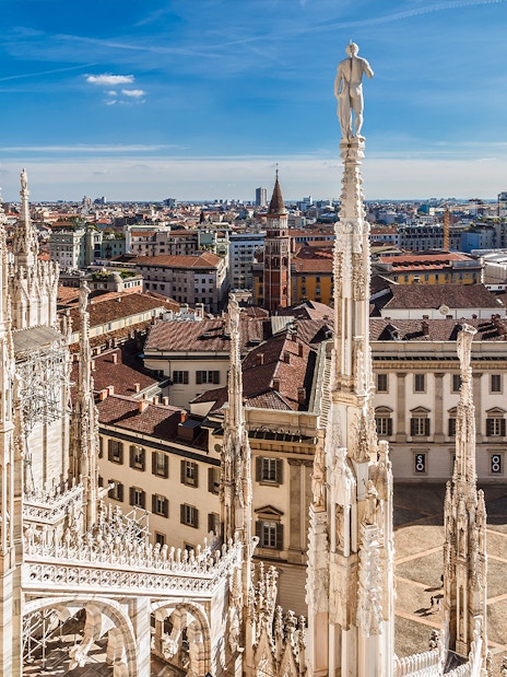Milan Cathedral rooftop view with cityscape and Italian flag.