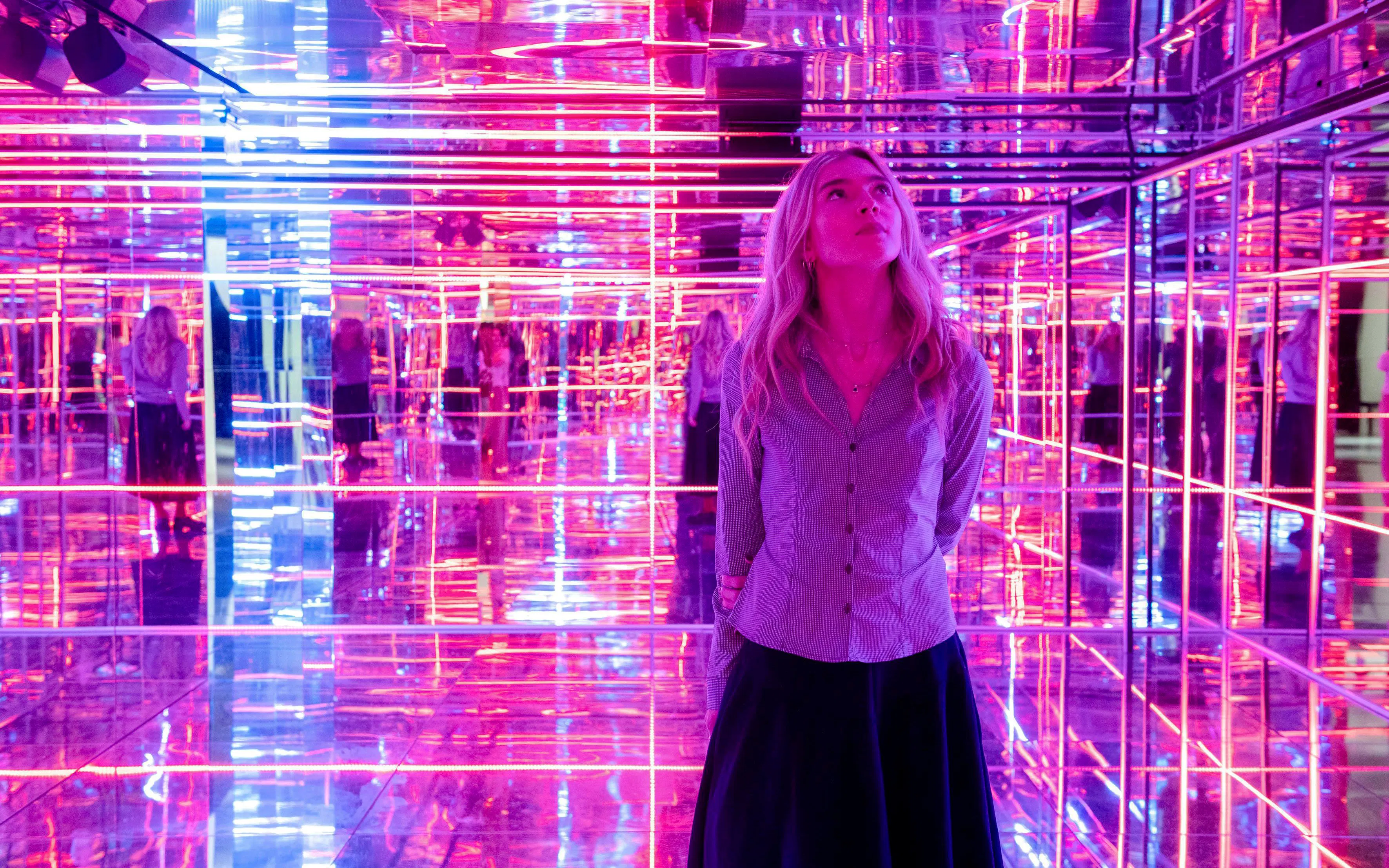 Visitor exploring neon-lit mirrored room at Moco Museum, London.