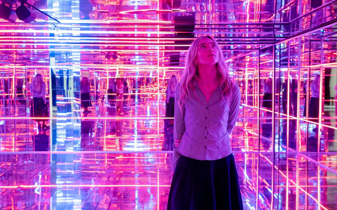Visitor exploring neon-lit mirrored room at Moco Museum, London.