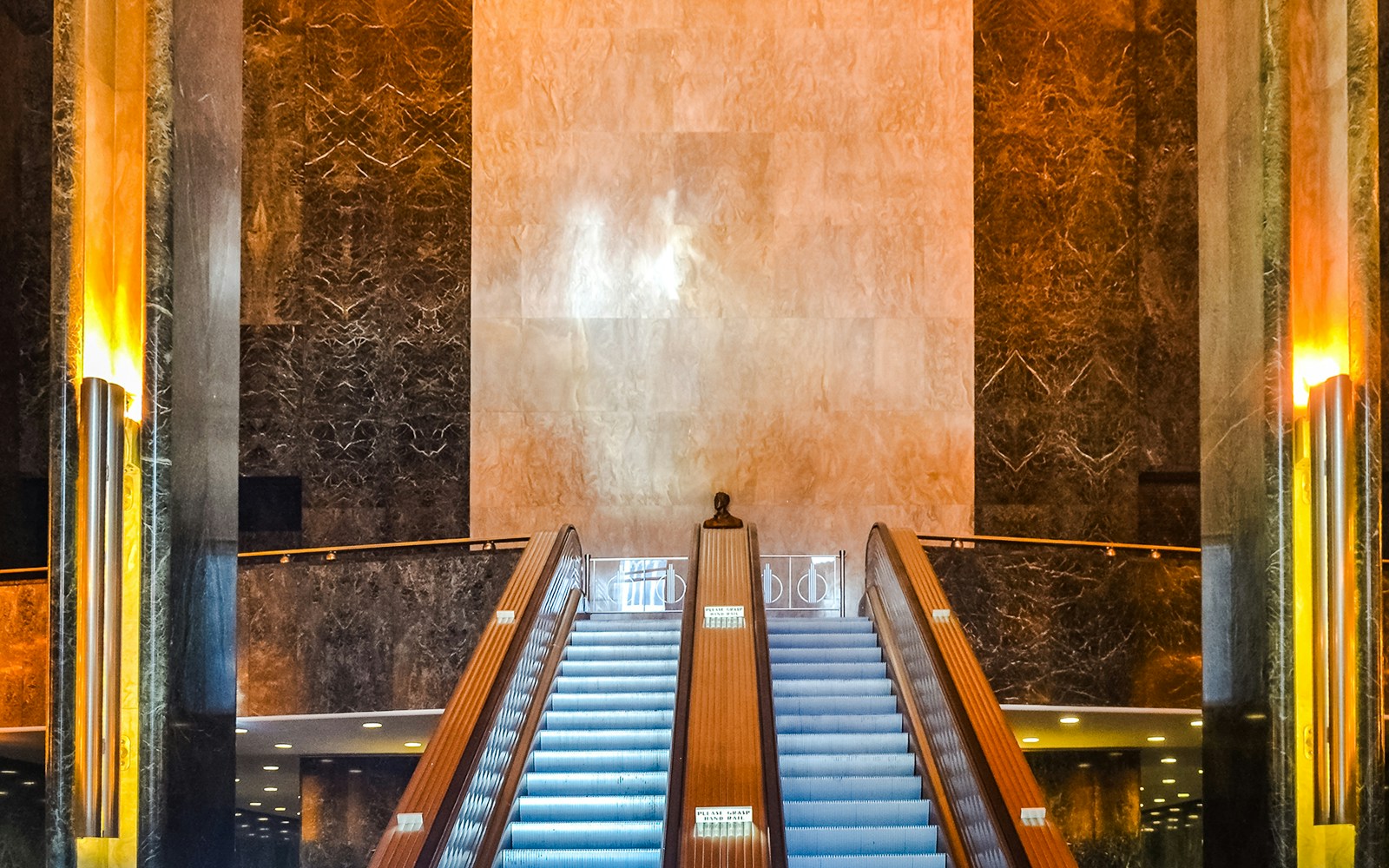Escalator in Rockefeller Center hall, New York City, with marble walls and warm lighting.