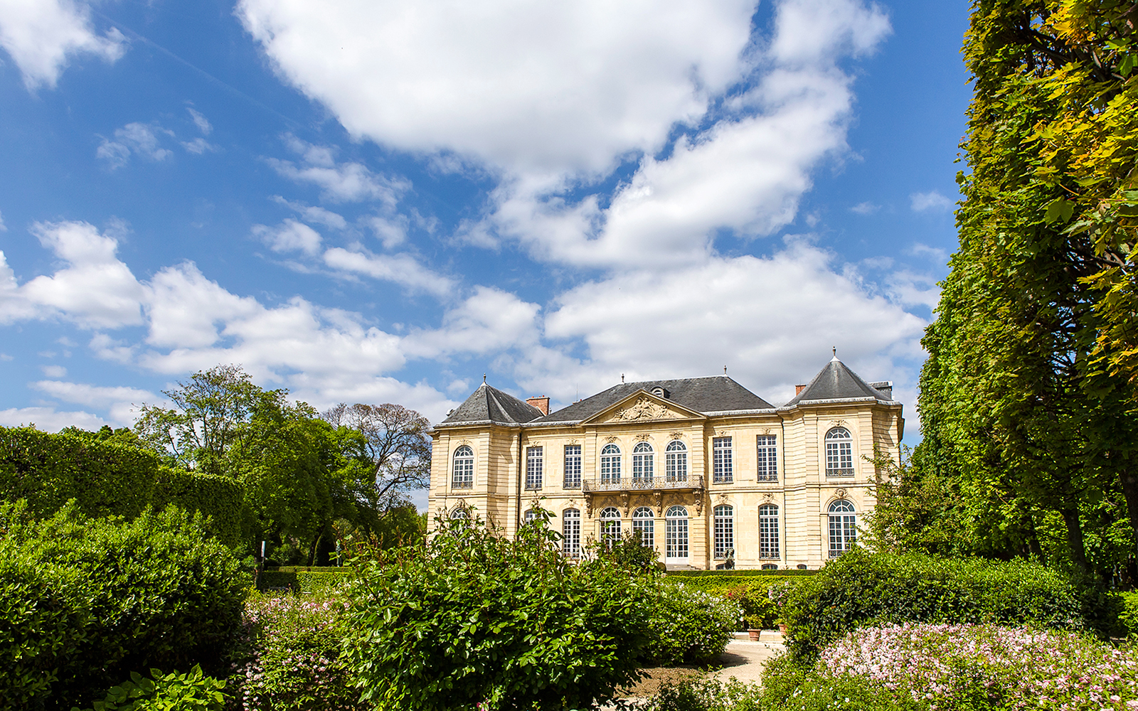 Hôtel Biron surrounded by lush gardens under a blue sky.