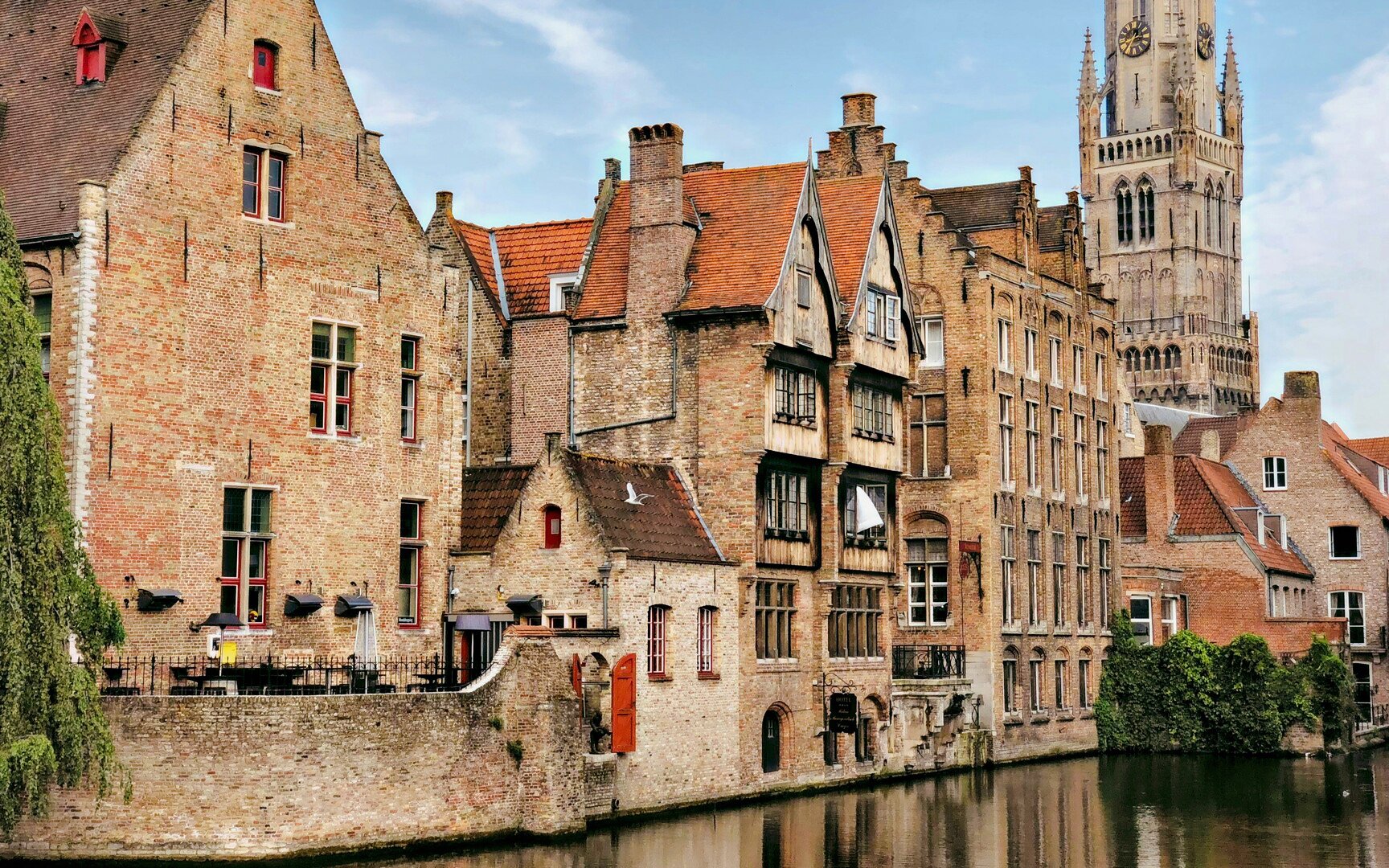 Canal view in Bruges historic center with Belfry of Bruges in the background.