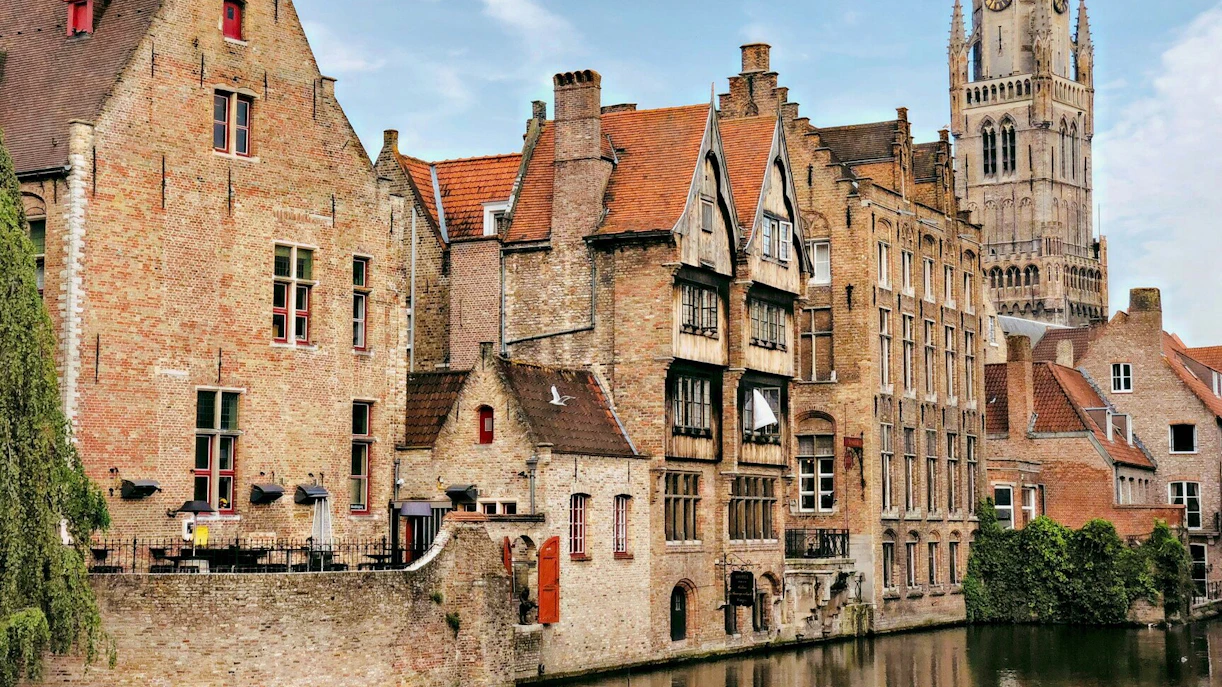 Canal view in Bruges historic center with Belfry of Bruges in the background.