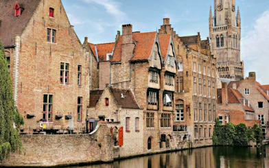 Canal view in Bruges historic center with Belfry of Bruges in the background.
