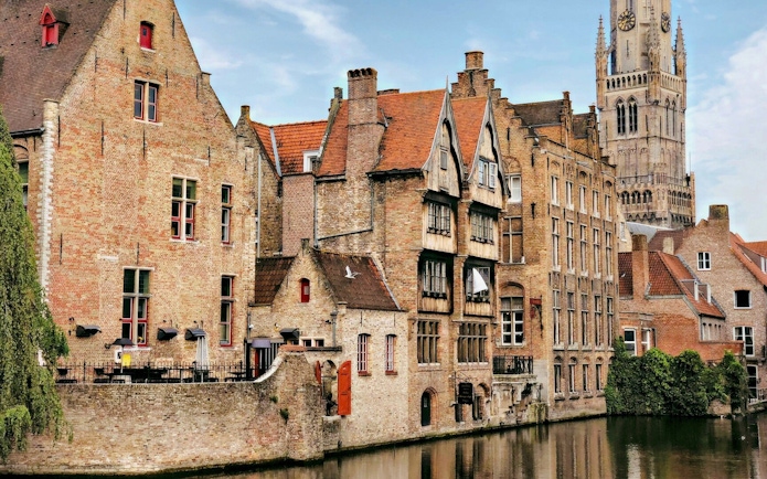 Canal view in Bruges historic center with Belfry of Bruges in the background.
