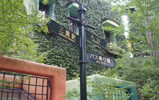 Signpost at Studio Ghibli Museum entrance in Mitaka, Japan, surrounded by greenery.