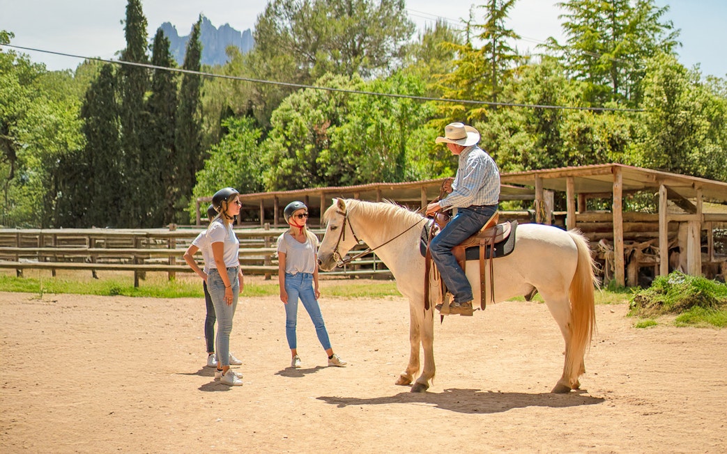 Guide instructing tourists at horse track on riding techniques.
