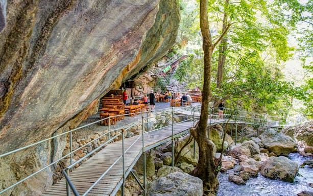 Wooden walkway and dining area under rock formations on a family rafting tour near Antalya.