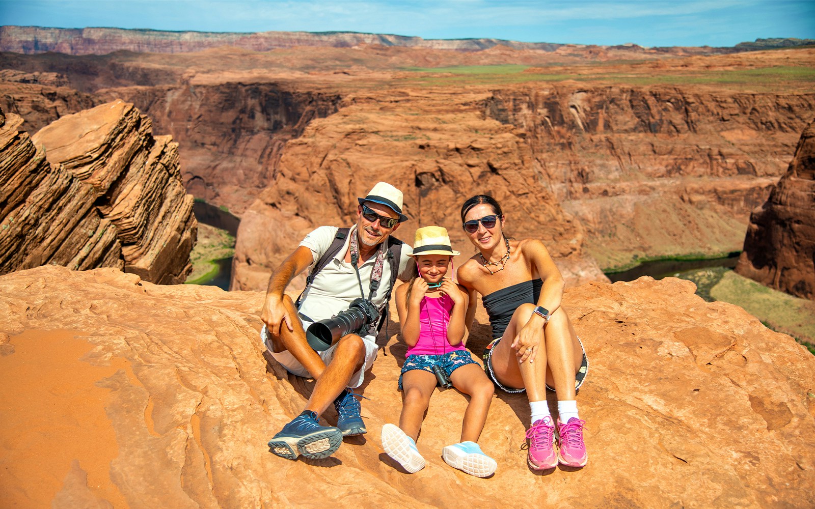 Family sitting on red rock cliff at Horseshoe Bend, Arizona, during Secret Antelope Canyon tour.