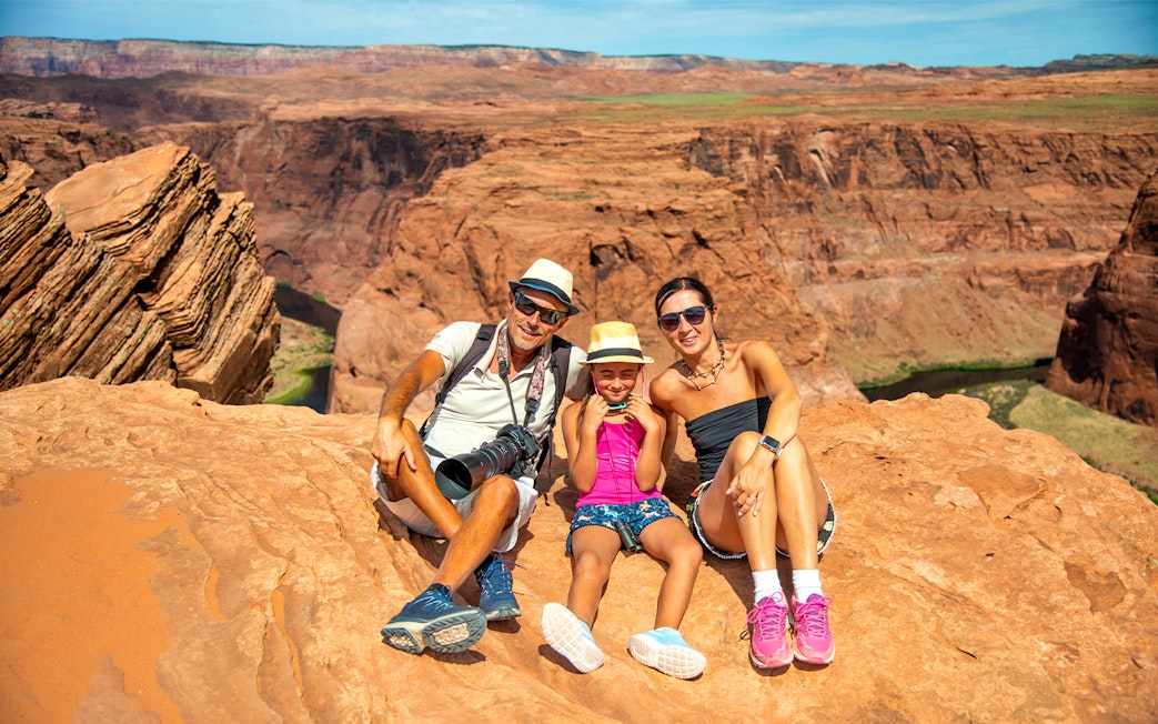 Family sitting on red rock cliff at Horseshoe Bend, Arizona, during Secret Antelope Canyon tour.