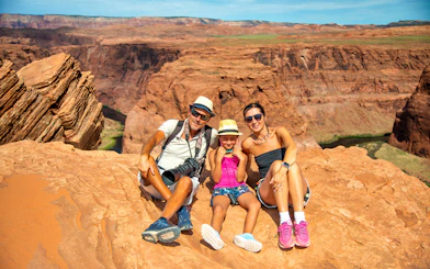 Family sitting on red rock cliff at Horseshoe Bend, Arizona, during Secret Antelope Canyon tour.