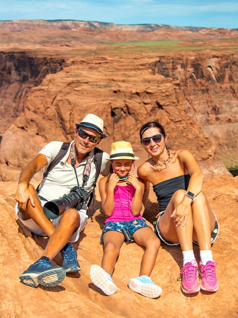 Family sitting on red rock cliff at Horseshoe Bend, Arizona, during Secret Antelope Canyon tour.