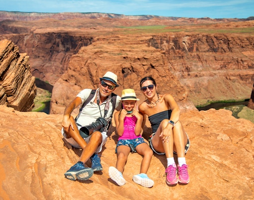 Family sitting on red rock cliff at Horseshoe Bend, Arizona, during Secret Antelope Canyon tour.