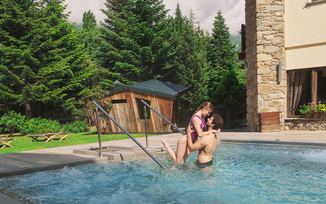 Couple enjoying outdoor pool at QC Terme Pré Saint Didier with lush greenery.