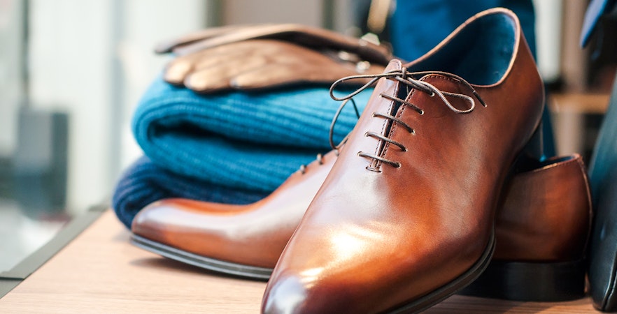 Brown leather dress shoes and folded blue sweater, suitable for Moulin Rouge dress code.