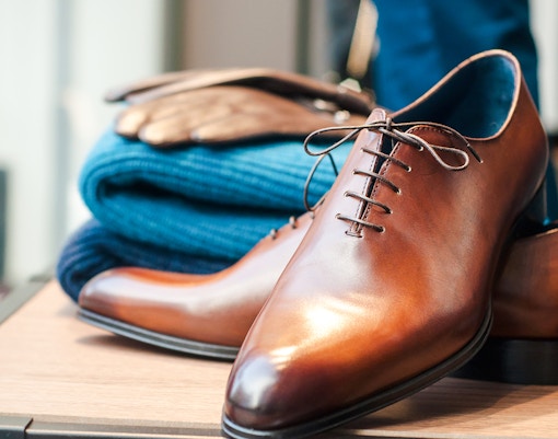 Brown leather dress shoes and folded blue sweater, suitable for Moulin Rouge dress code.