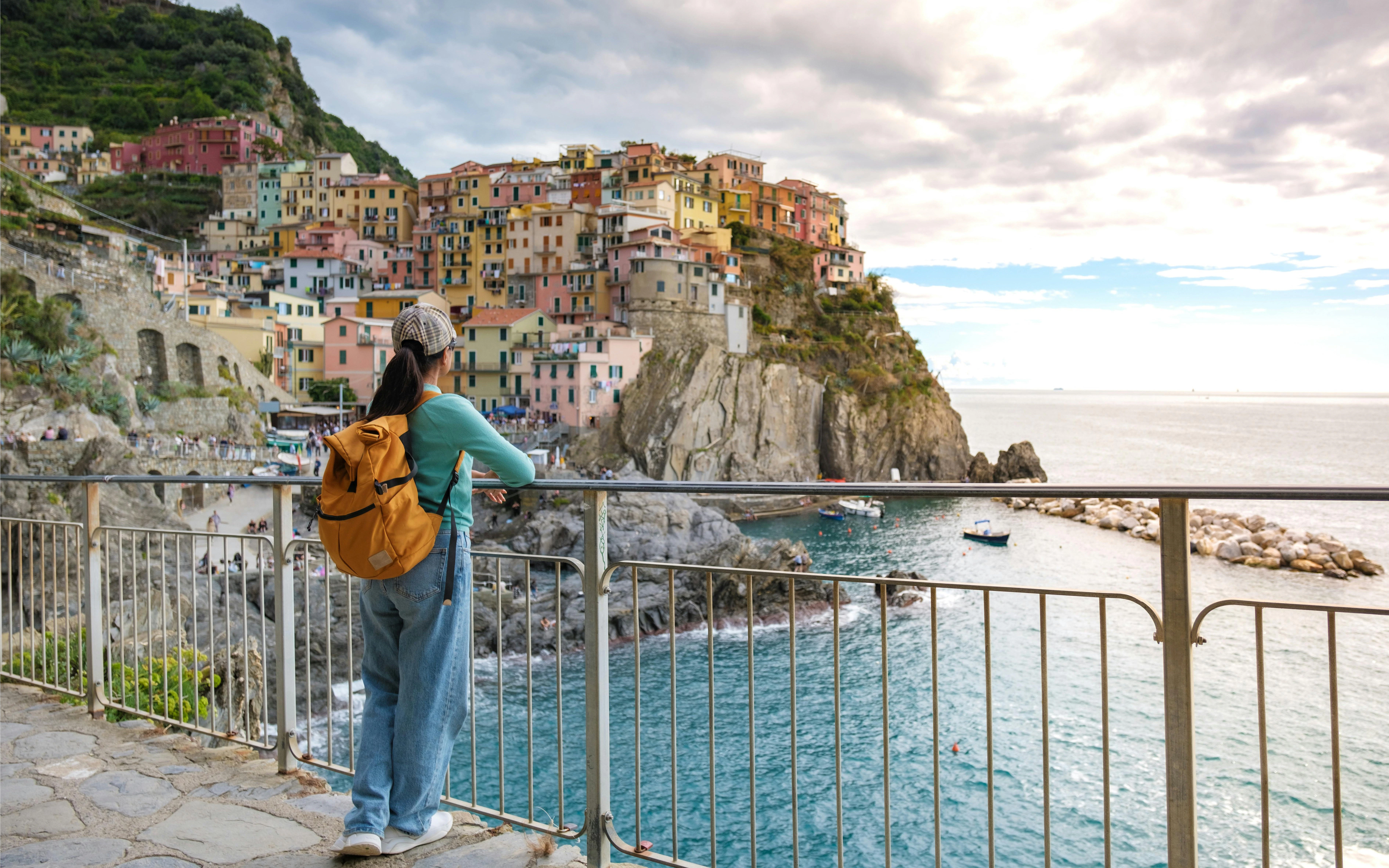 Traveler overlooking Manarola's colorful cliffside buildings and sea in Cinque Terre during evening.