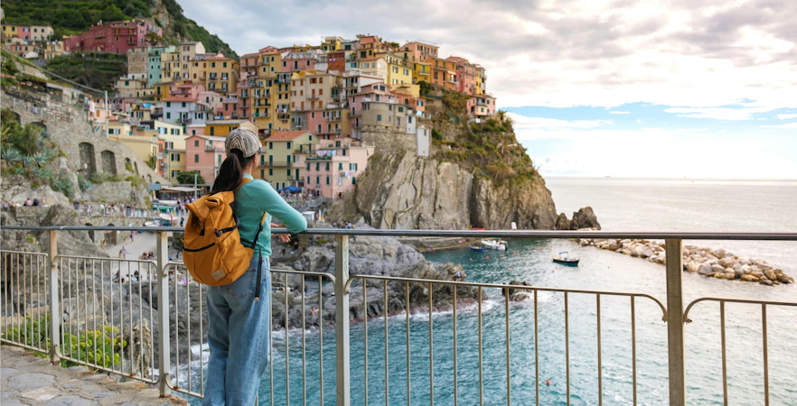 Traveler overlooking Manarola's colorful cliffside buildings and sea in Cinque Terre during evening.
