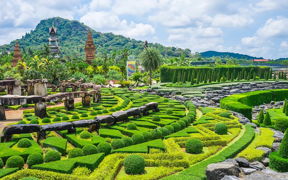 Nong Nooch Tropical Garden's manicured hedges and stone structures with mountain backdrop.