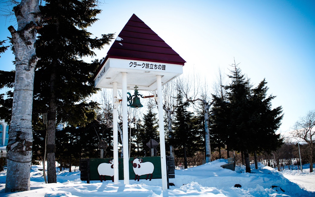 Clark's Departure Bell monument at Asahiyama Zoo, Hokkaido, Japan, surrounded by snow and trees.