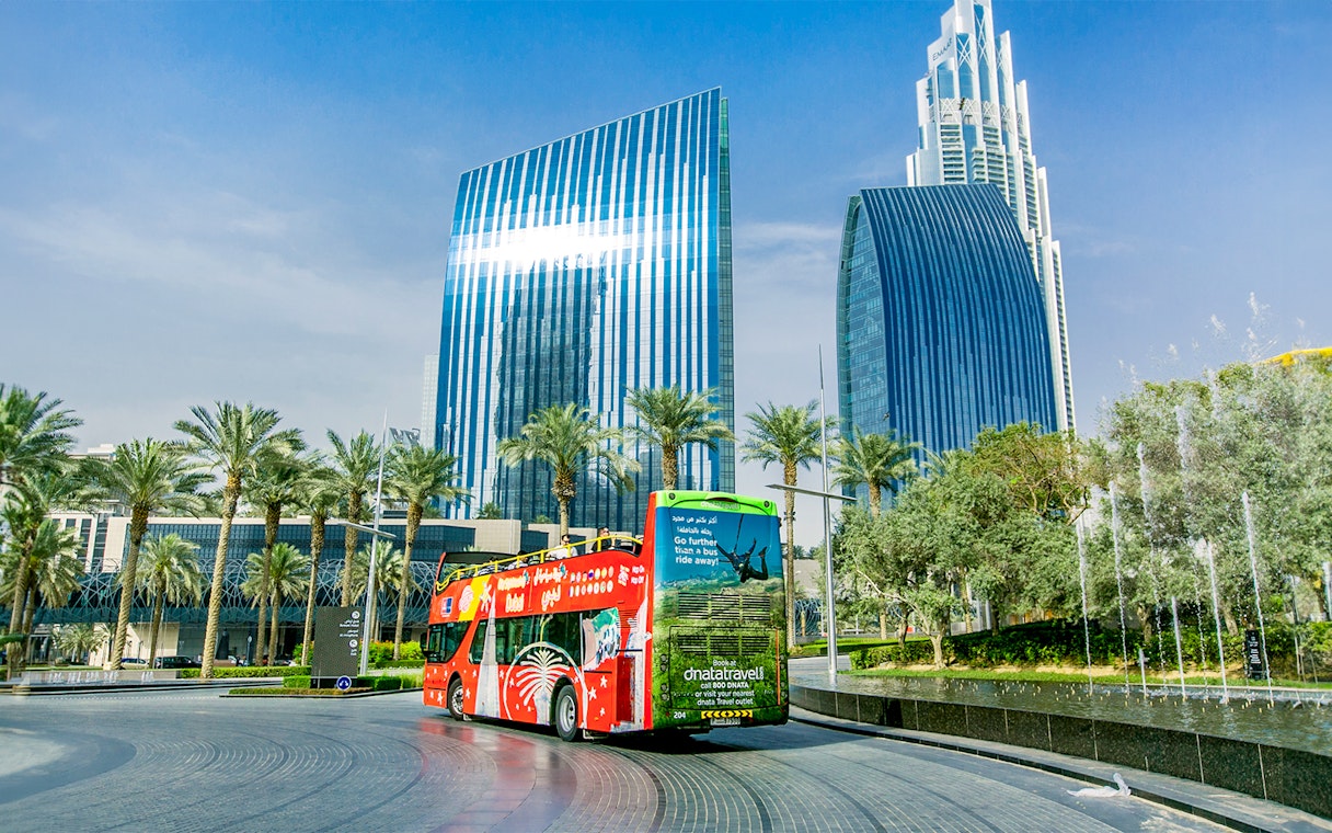 Open-top tour bus near modern skyscrapers in Dubai on Hop-On Hop-Off Tour with Al Seef Dhow Cruise.