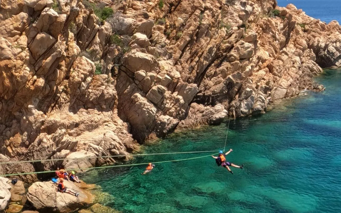 Coasteering adventure along rocky cliffs in Costa Smeralda, Porto Cervo, with participants in safety gear.