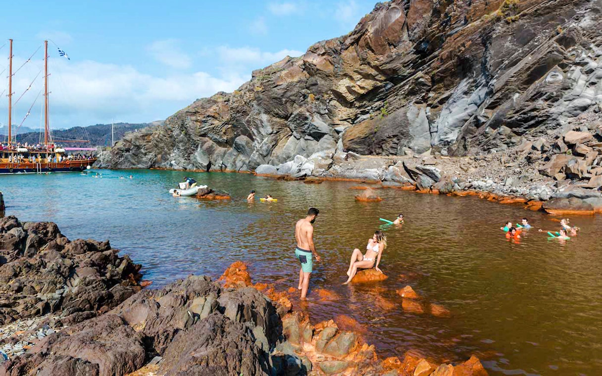 Guests swimming near rocky shore at Santorini Volcanic Island.