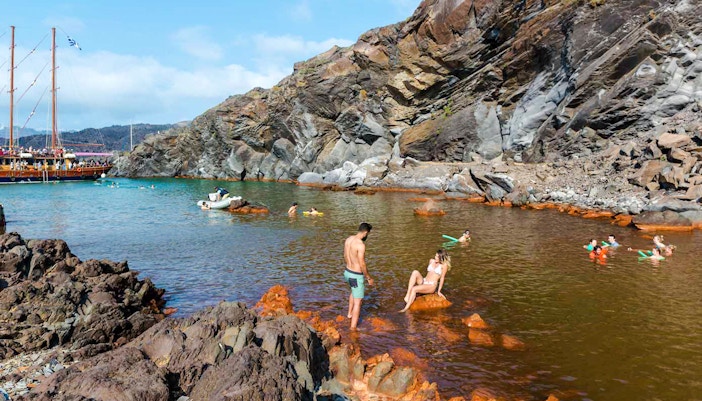 Guests swimming near rocky shore at Santorini Volcanic Island.