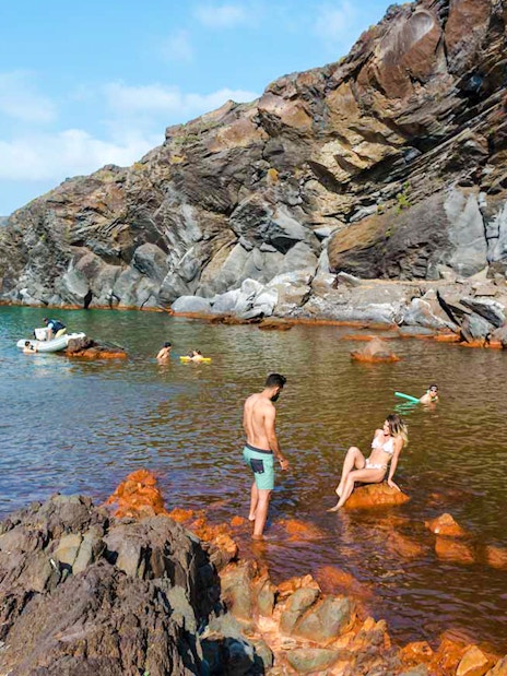 Guests swimming near rocky shore at Santorini Volcanic Island.