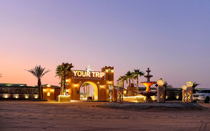Entrance to evening desert safari with decorative lights and palm trees.