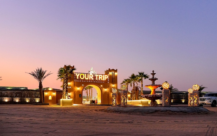 Entrance to evening desert safari with decorative lights and palm trees.
