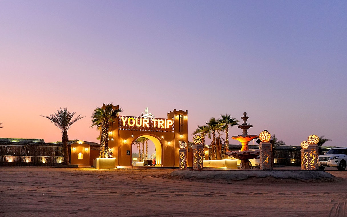 Entrance to evening desert safari with decorative lights and palm trees.