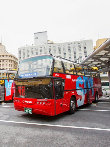 Red double-decker bus for Kyoto city tour parked at a station.