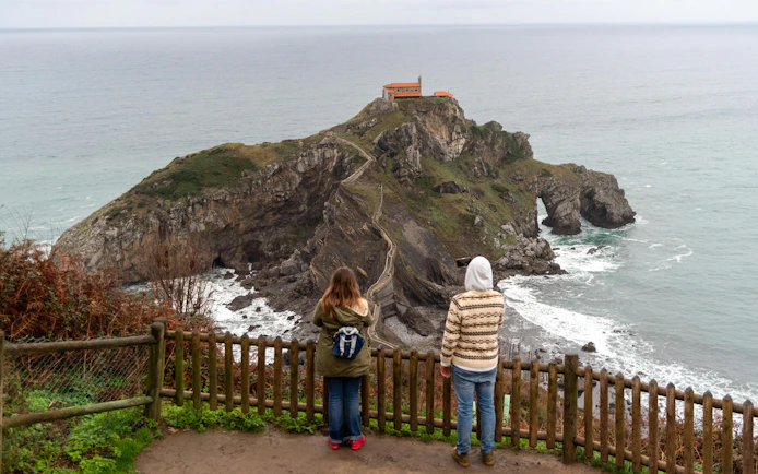 Tourists photographing San Juan de Gaztelugatxe hermitage on Basque coast.