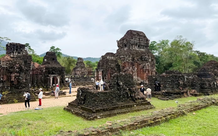 Ancient temple ruins at My Son Sanctuary, Quang Nam, Vietnam, with tourists exploring the site.