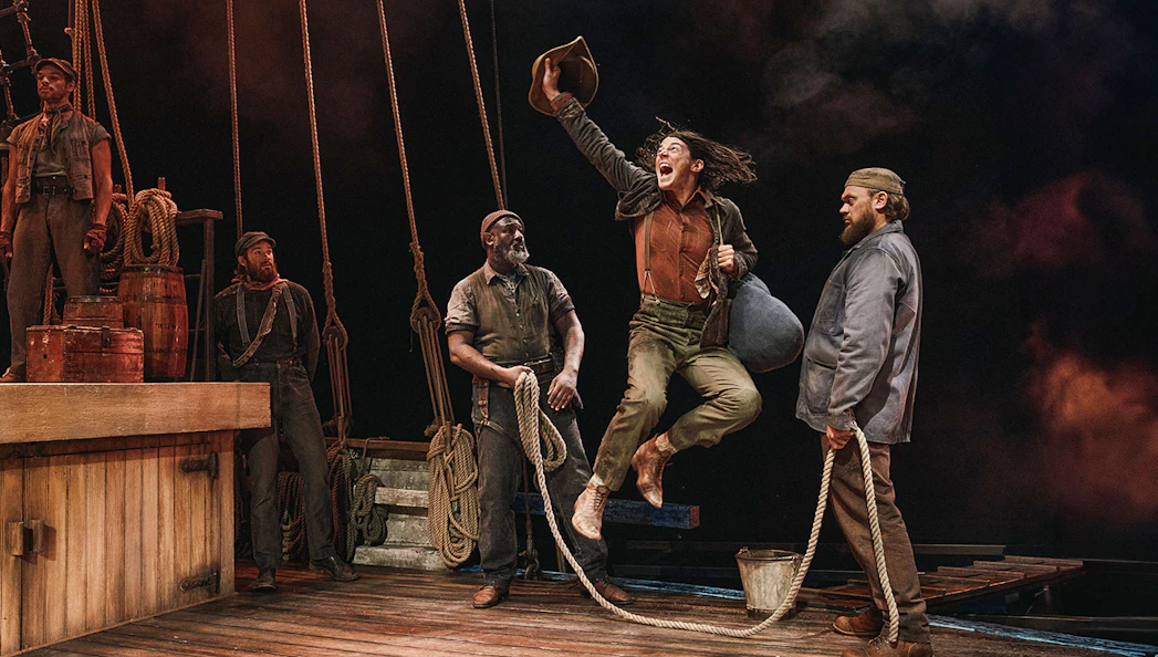 Sailors on a ship's deck, one jumping with joy, holding a hat, others watching.