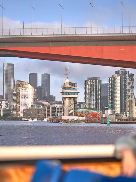 Melbourne skyline viewed from a river cruise under a bridge.