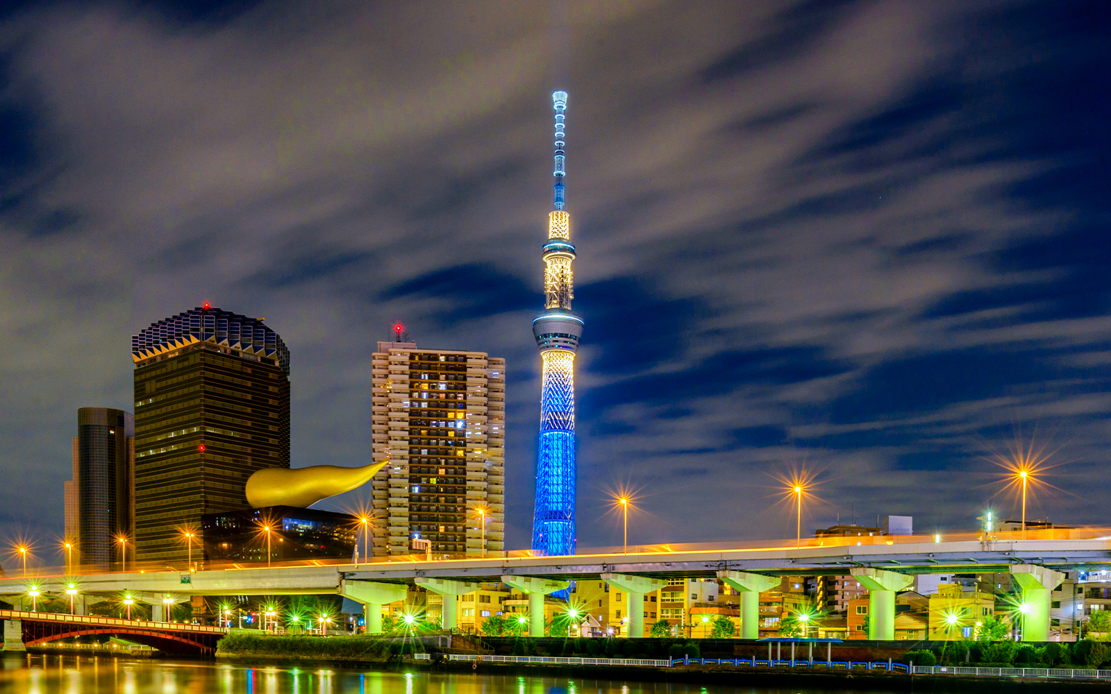 Tokyo SkyTree illuminated at night with city skyline and river in foreground.