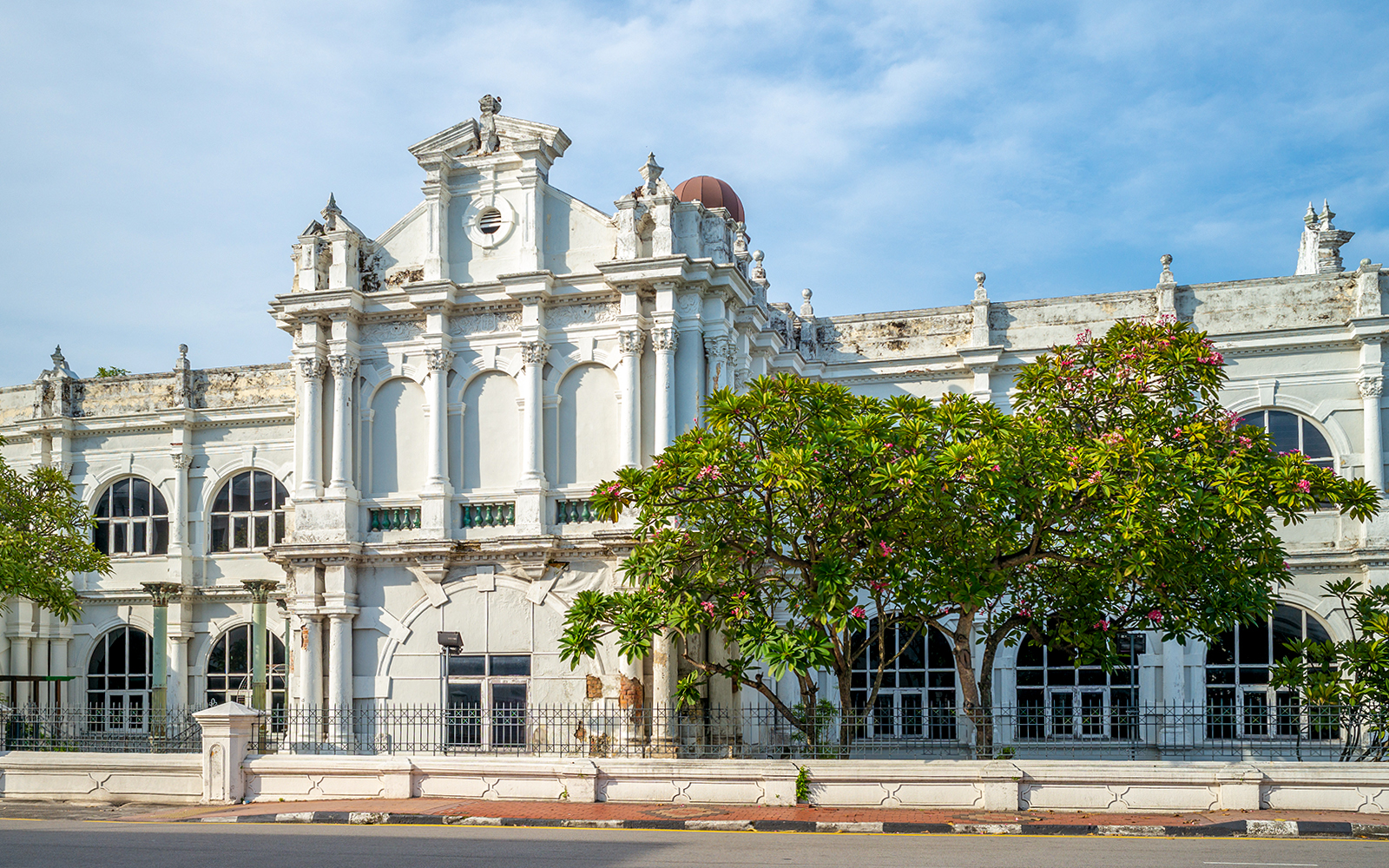 Historic facade of Penang State Museum and Art Gallery, Malaysia, with arched windows and lush greenery.