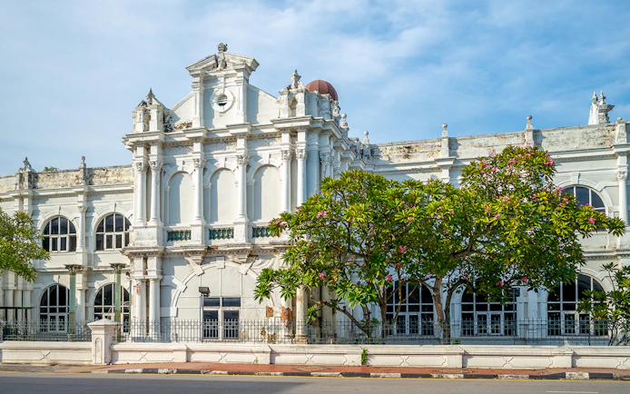Historic facade of Penang State Museum and Art Gallery, Malaysia, with arched windows and lush greenery.