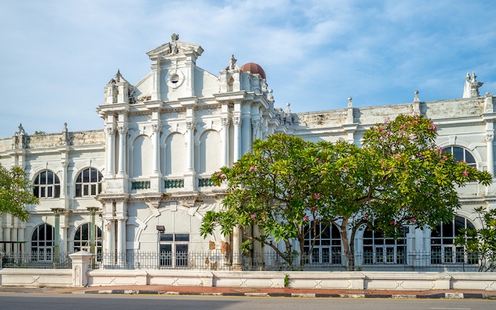 Historic facade of Penang State Museum and Art Gallery, Malaysia, with arched windows and lush greenery.