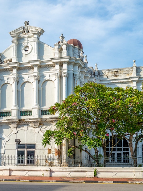 Historic facade of Penang State Museum and Art Gallery, Malaysia, with arched windows and lush greenery.