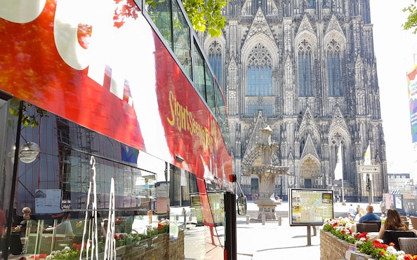 Hop on hop off bus near Cologne Cathedral with Gothic architecture in background.