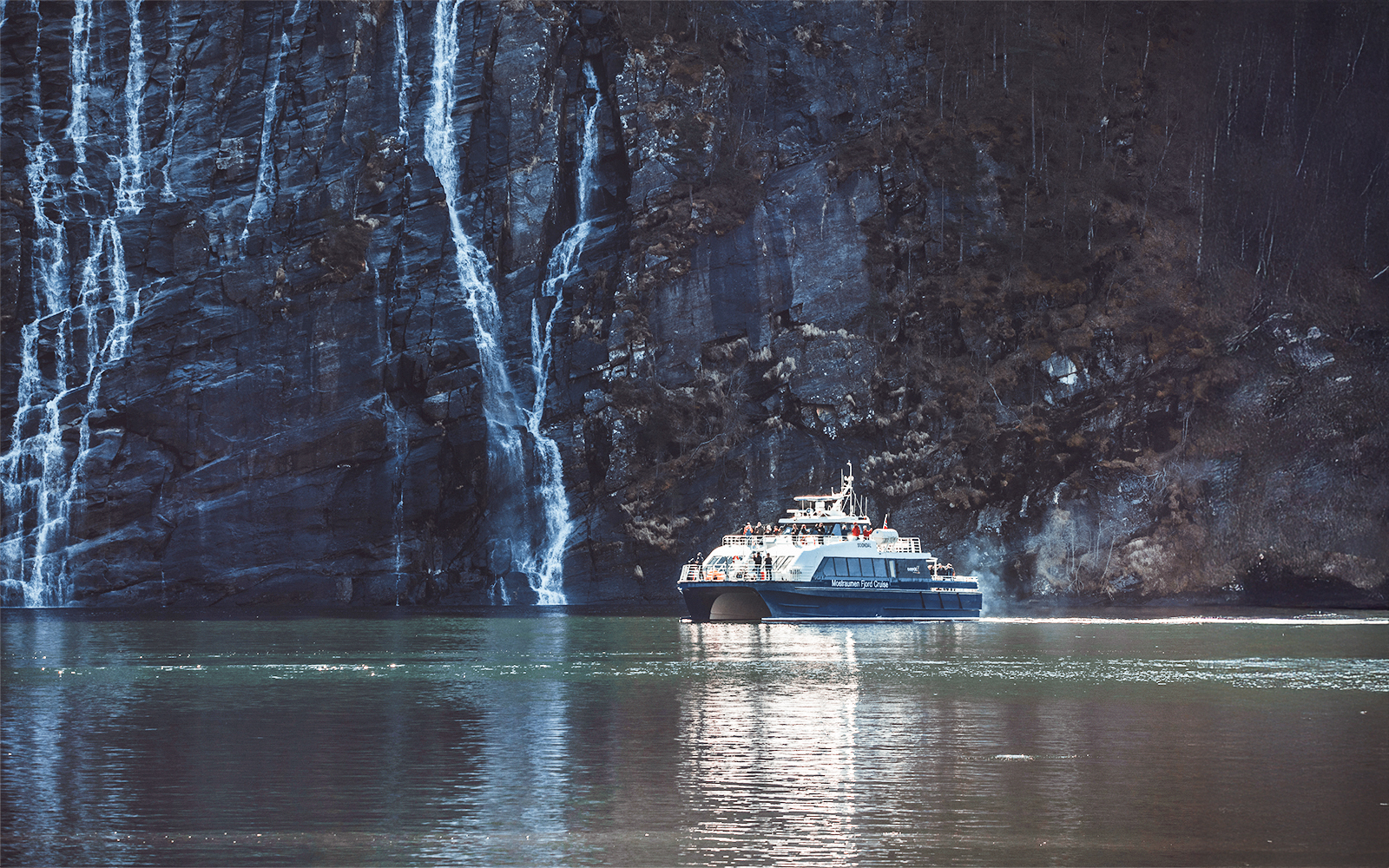 Boat cruising near waterfalls in Mostraumen Fjord, Norway.