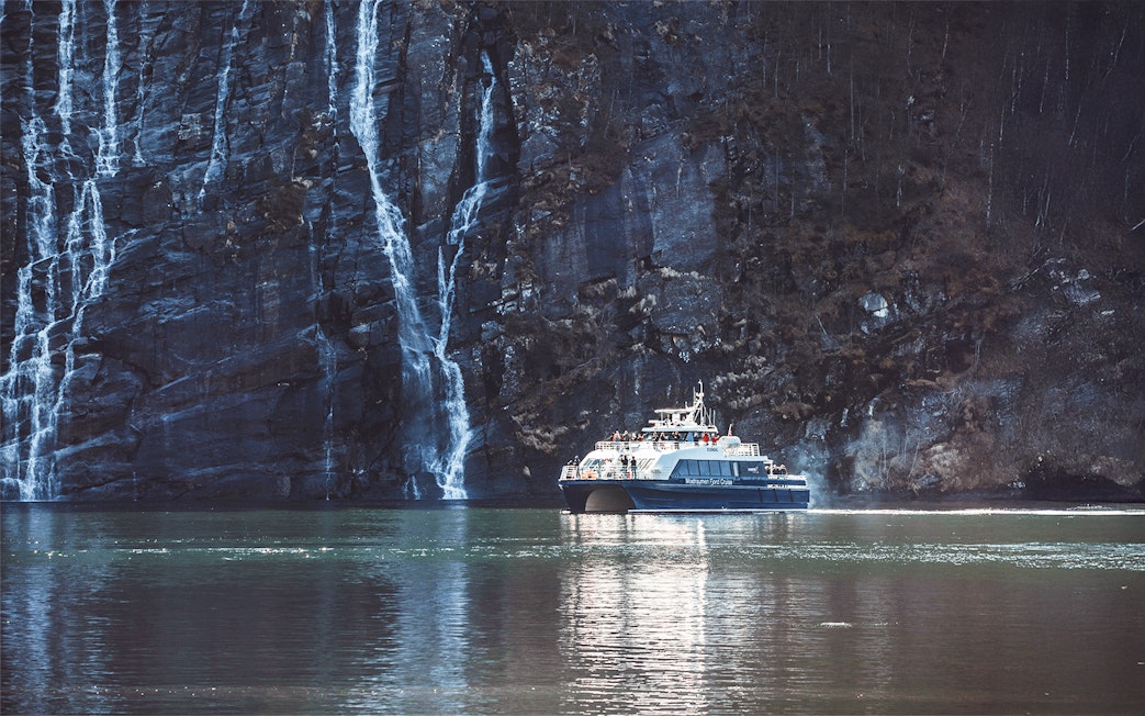 Boat cruising near waterfalls in Mostraumen Fjord, Norway.