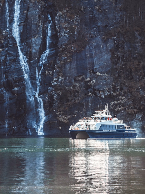 Boat cruising near waterfalls in Mostraumen Fjord, Norway.
